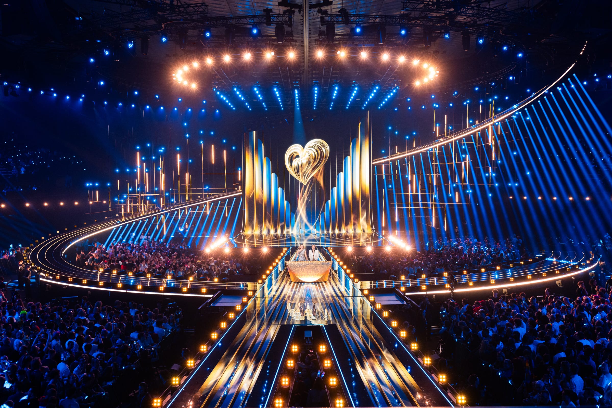 The Grand Final of the Eurovision Song Contest 2026 at Wiener Stadthalle: the hosts on the golden stage, blue light beams and a full arena